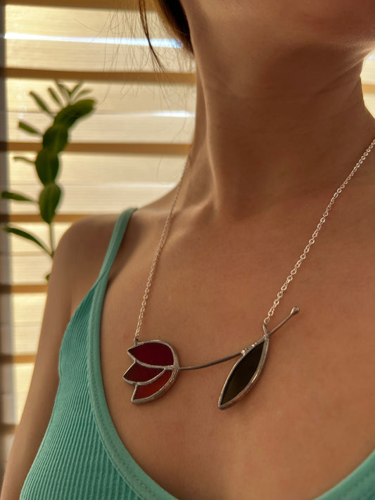 Close-up of handmade stained glass tulip necklace with red petals and minimalist design. Floral pendant on silver chain, nature-inspired look.