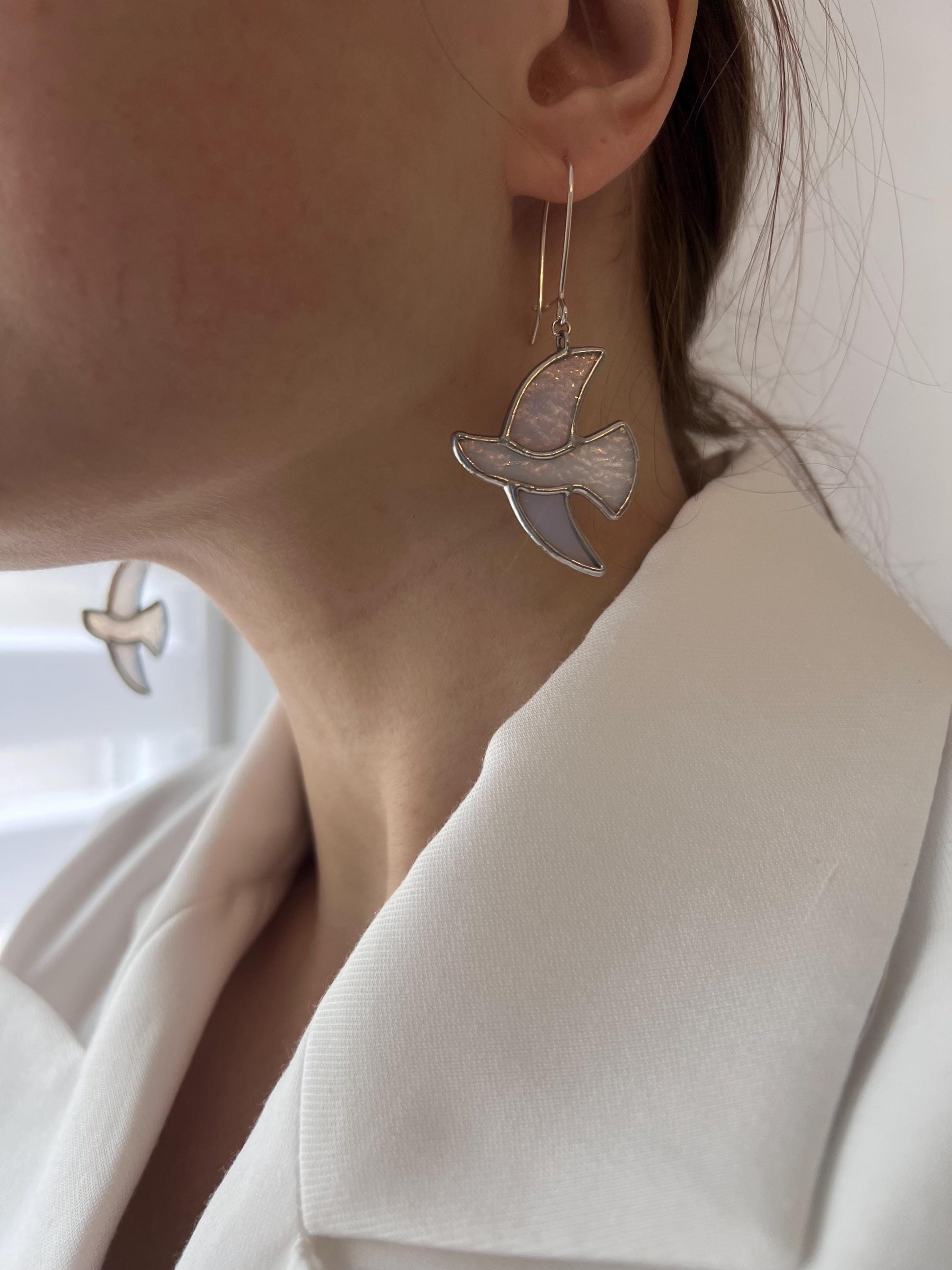 Handmade stained glass earrings shaped like white doves, photographed on model. Lightweight dangle bird earrings perfect for weddings, nature lovers, or meaningful gifts.