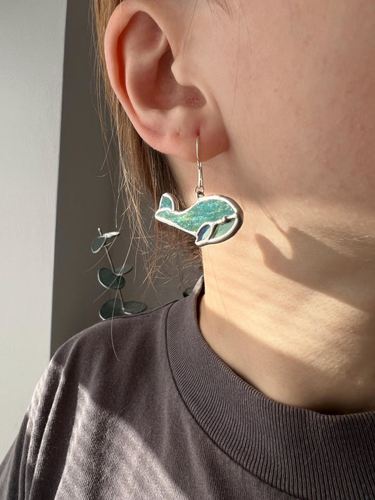 Stained glass baby whale earrings worn on ear, cute ocean dangle jewelry