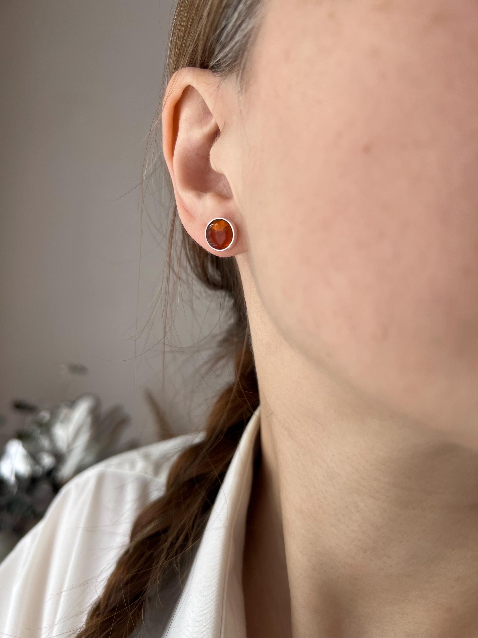 Caramel fused glass stud earrings on ear in warm light, small glossy round shape, minimalist warm-tone jewelry.