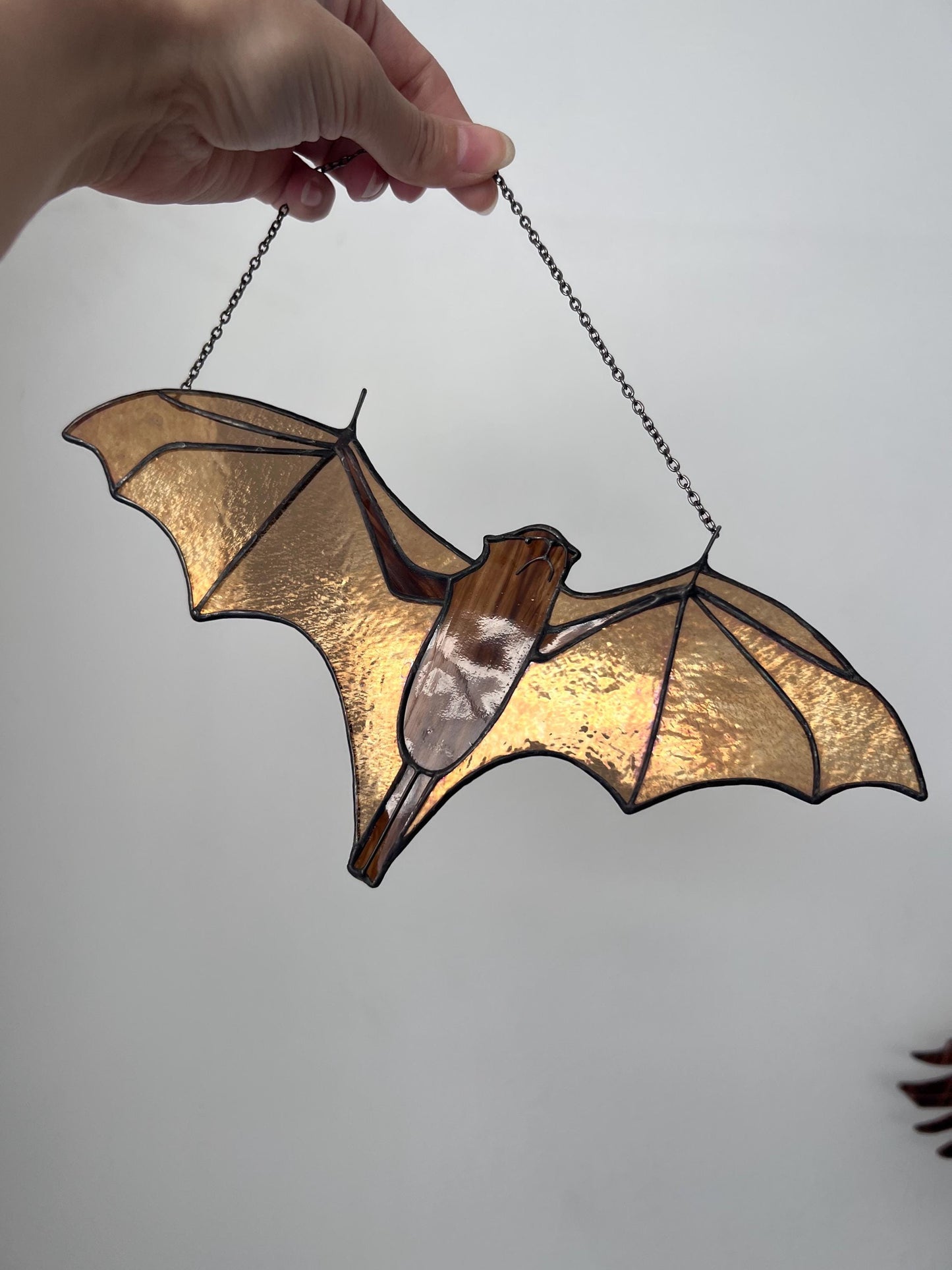 Handmade stained glass bat ornament in amber and brown tones hanging near a window, glowing in warm sunlight