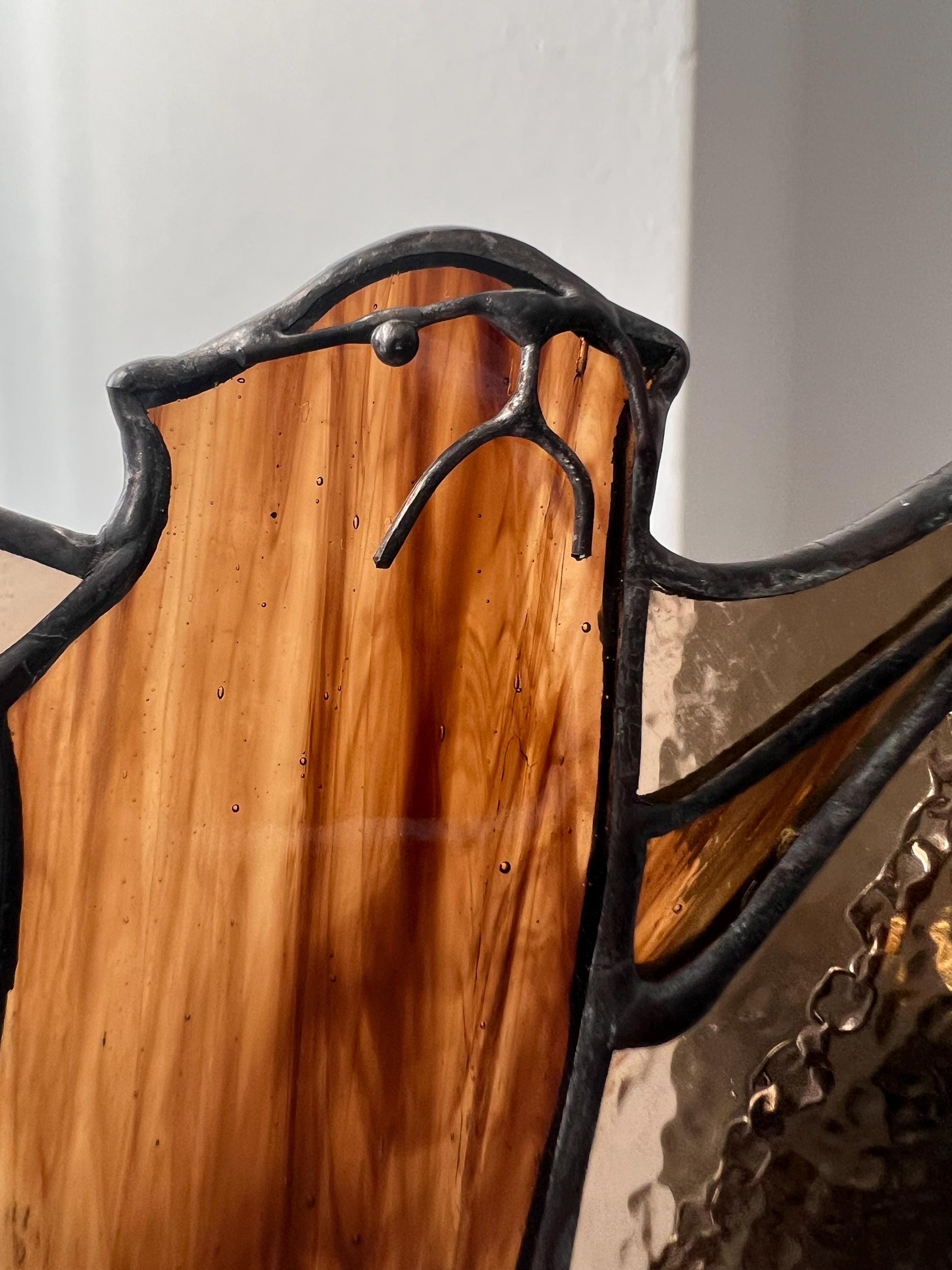 stained glass decoration in the form of a bat in amber and brown tones, the head is depicted in close-up, demonstrating small handmade details
