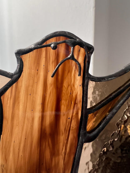 stained glass decoration in the form of a bat in amber and brown tones, the head is depicted in close-up, demonstrating small handmade details