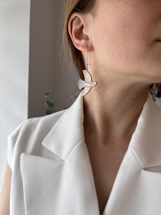 Handmade stained glass earrings shaped like white doves, photographed on model. Lightweight dangle bird earrings perfect for weddings, nature lovers, or meaningful gifts.