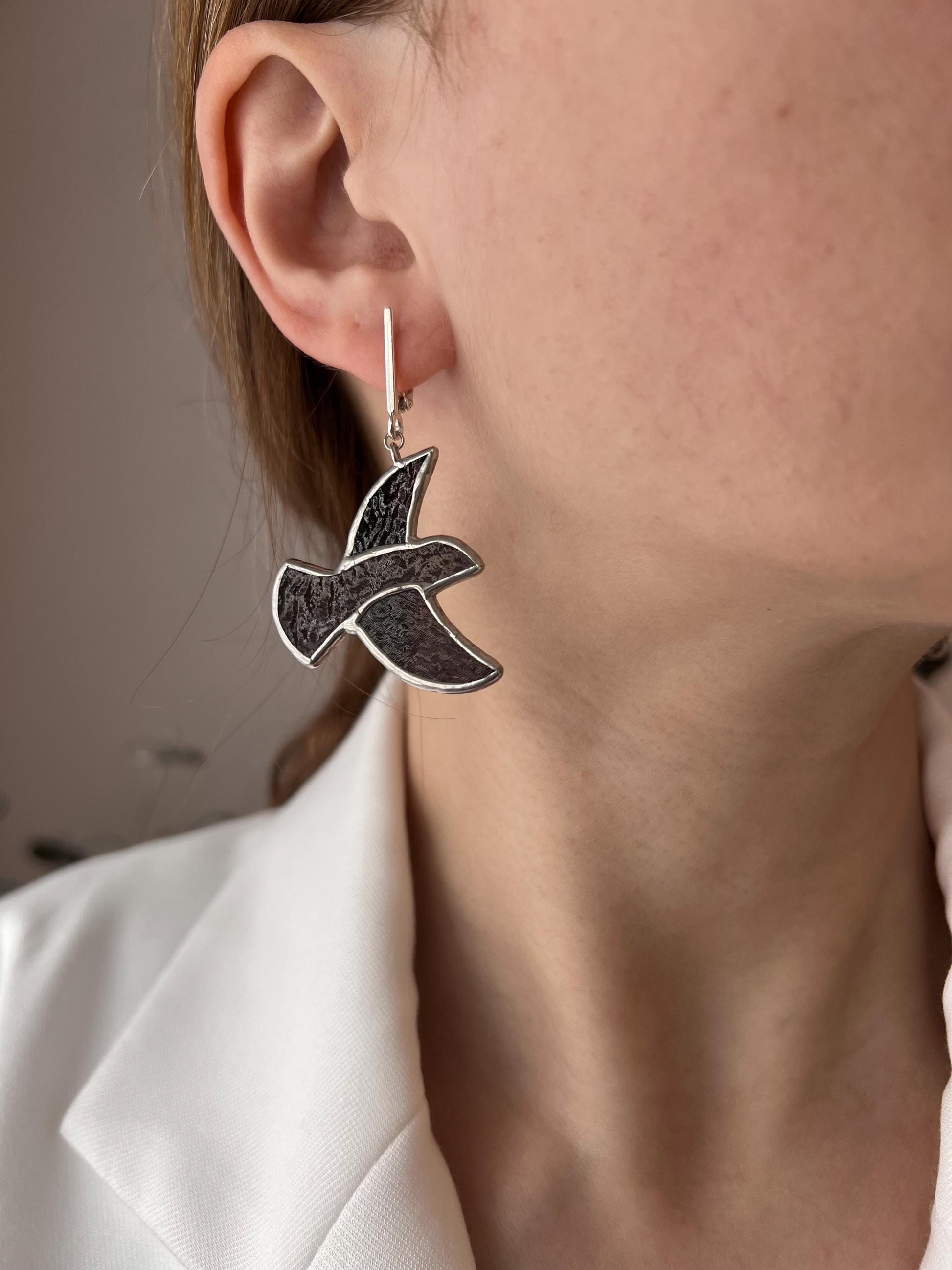 Close-up of a woman wearing handmade stained glass earrings in the shape of a brown bird – lightweight dangle earrings inspired by nature.