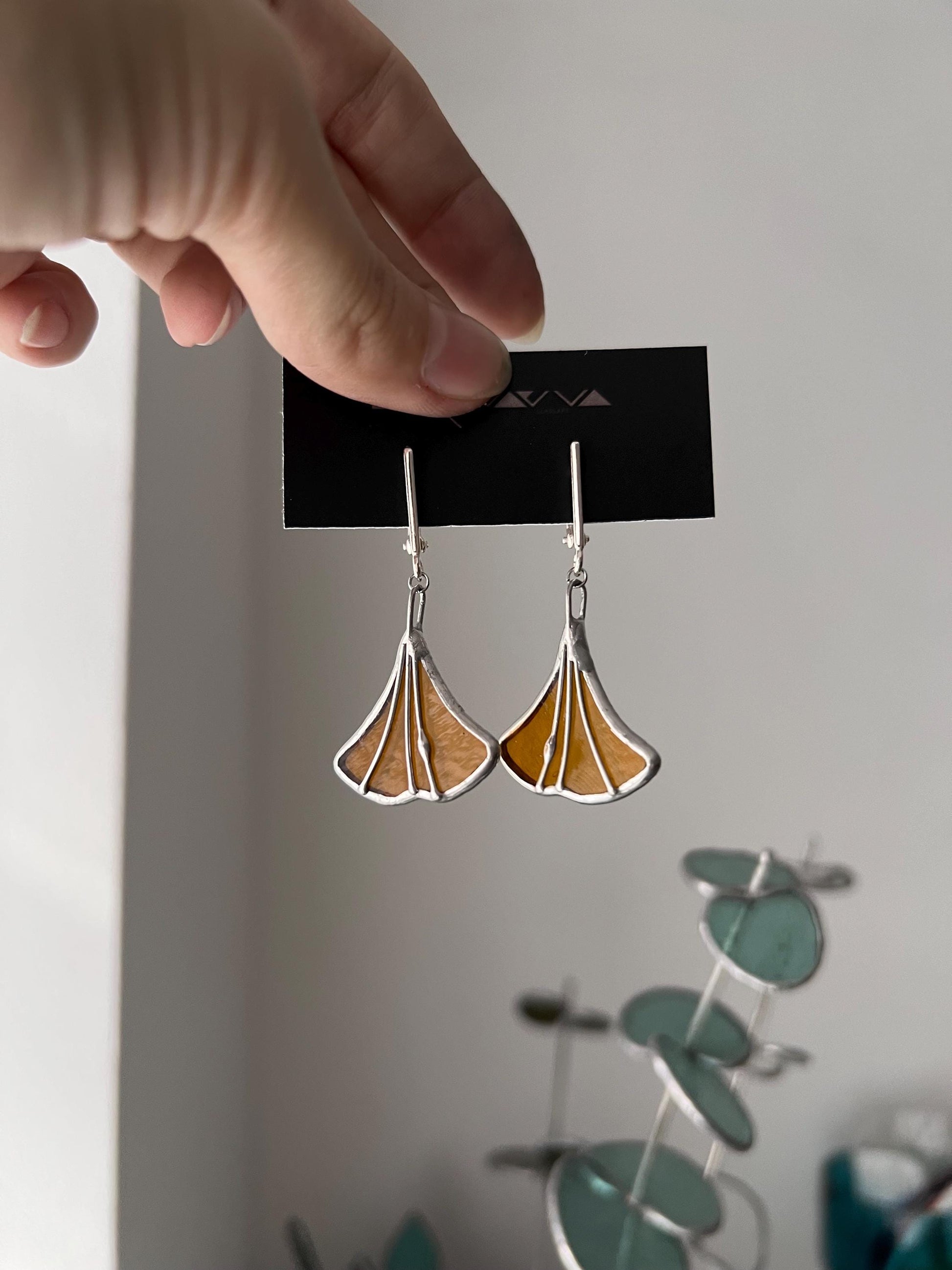 Handmade stained glass earrings shaped like ginkgo leaves, warm brown color with silver findings, nature-inspired dangle design.