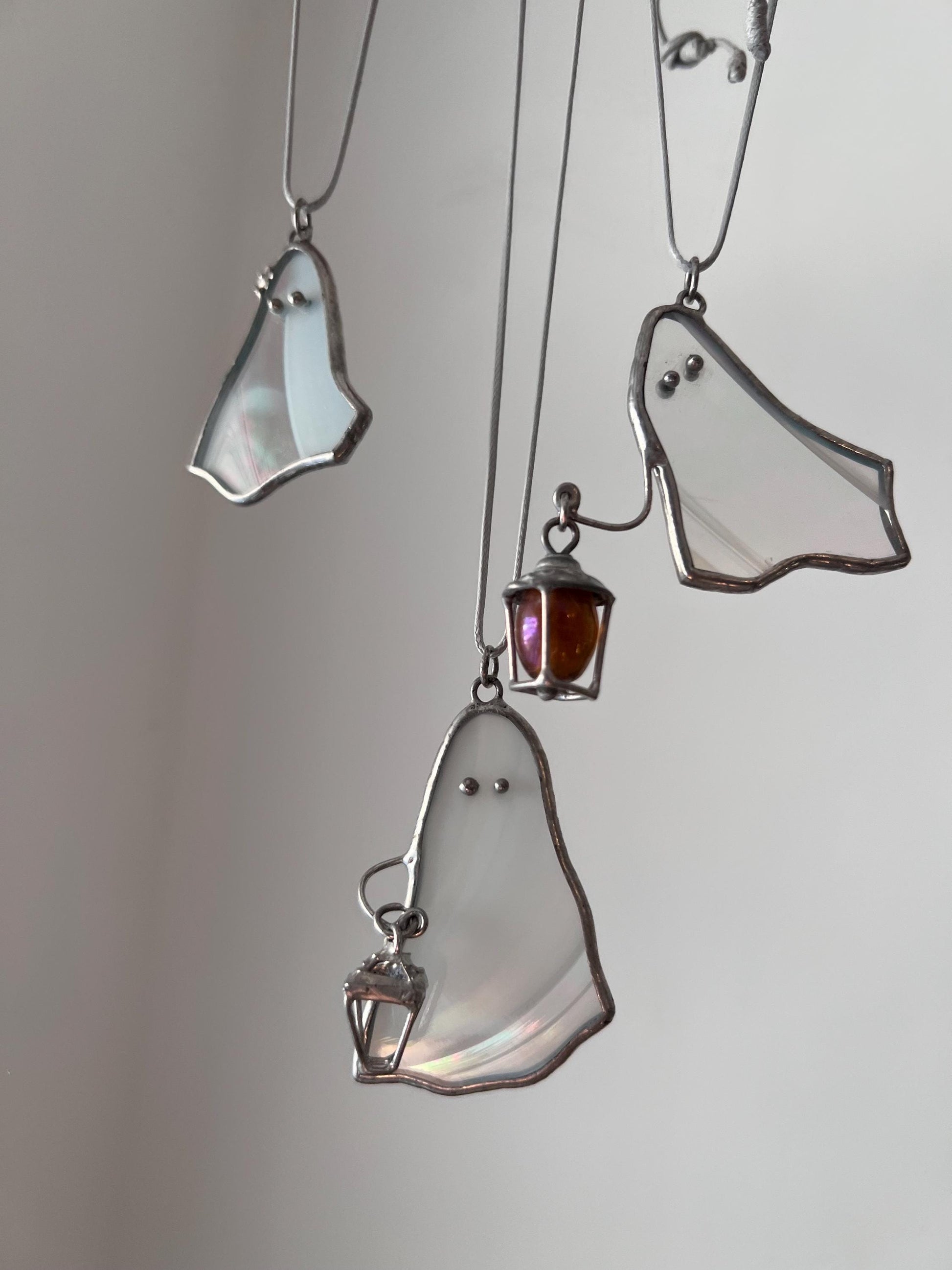 Three white stained glass ghost pendants hanging together, two holding a lantern