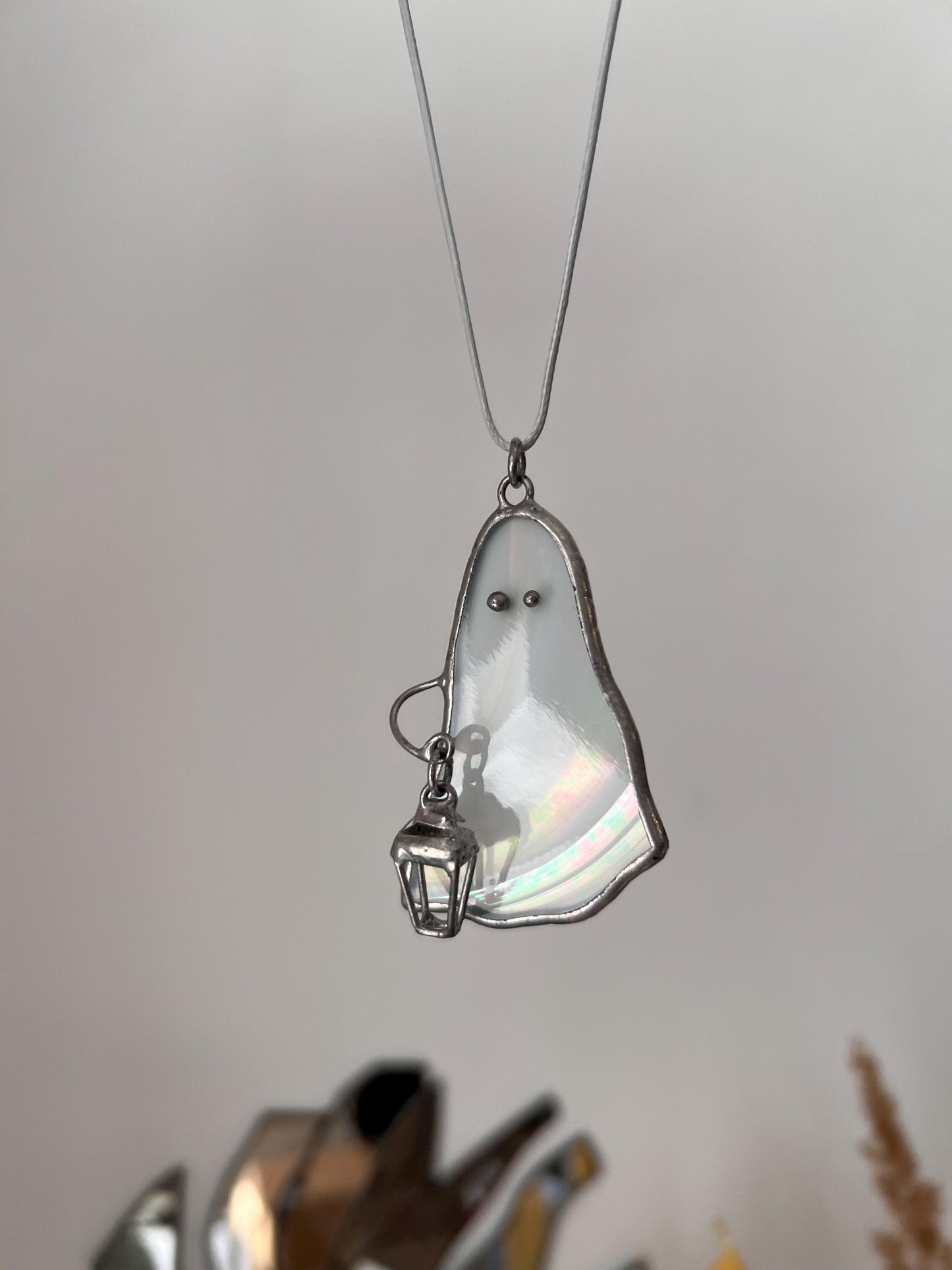 Handmade stained glass ghost pendant with iridescent effect hanging on a cotton