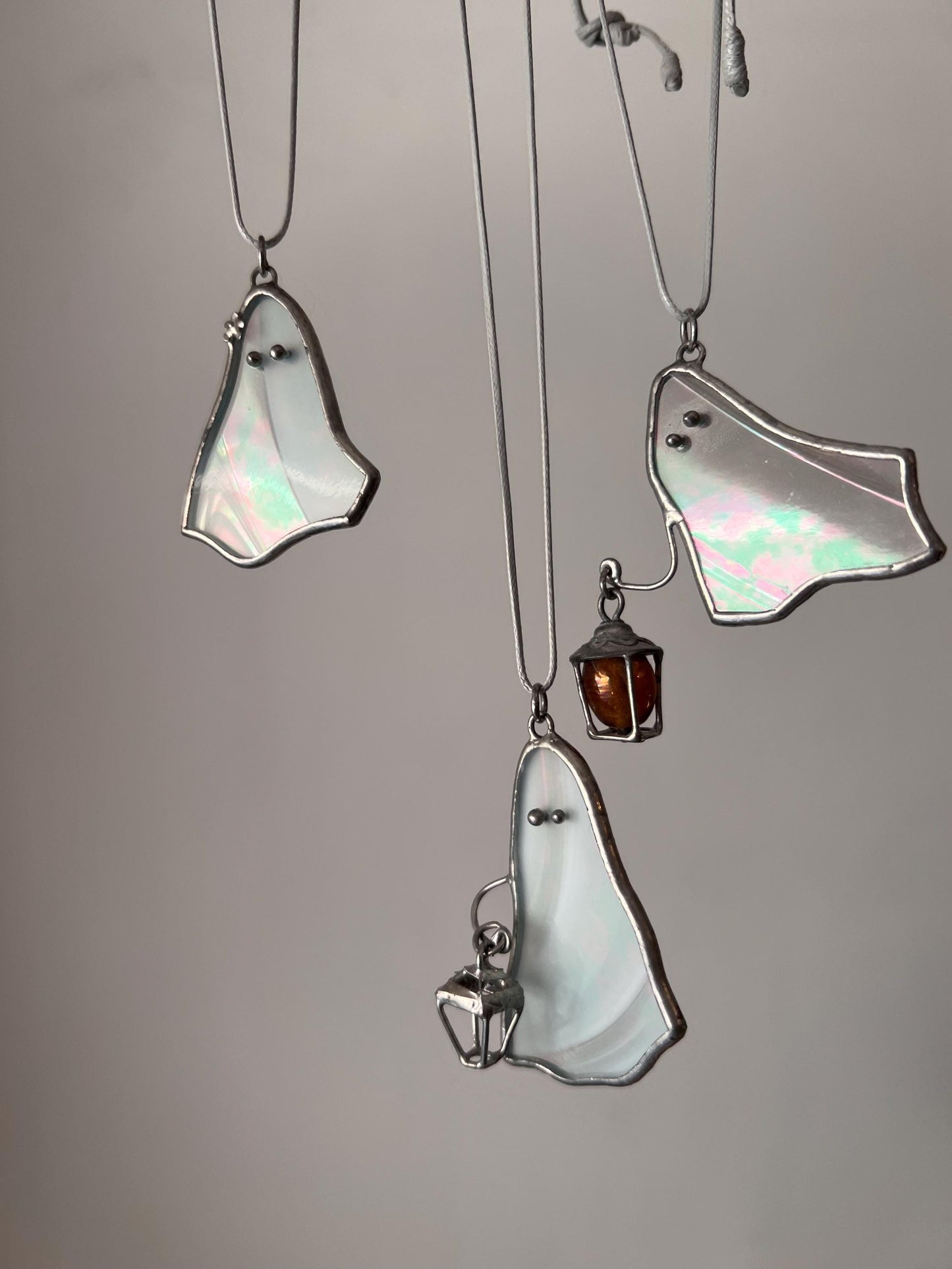 Three white stained glass ghost pendants hanging together, two holding a lantern