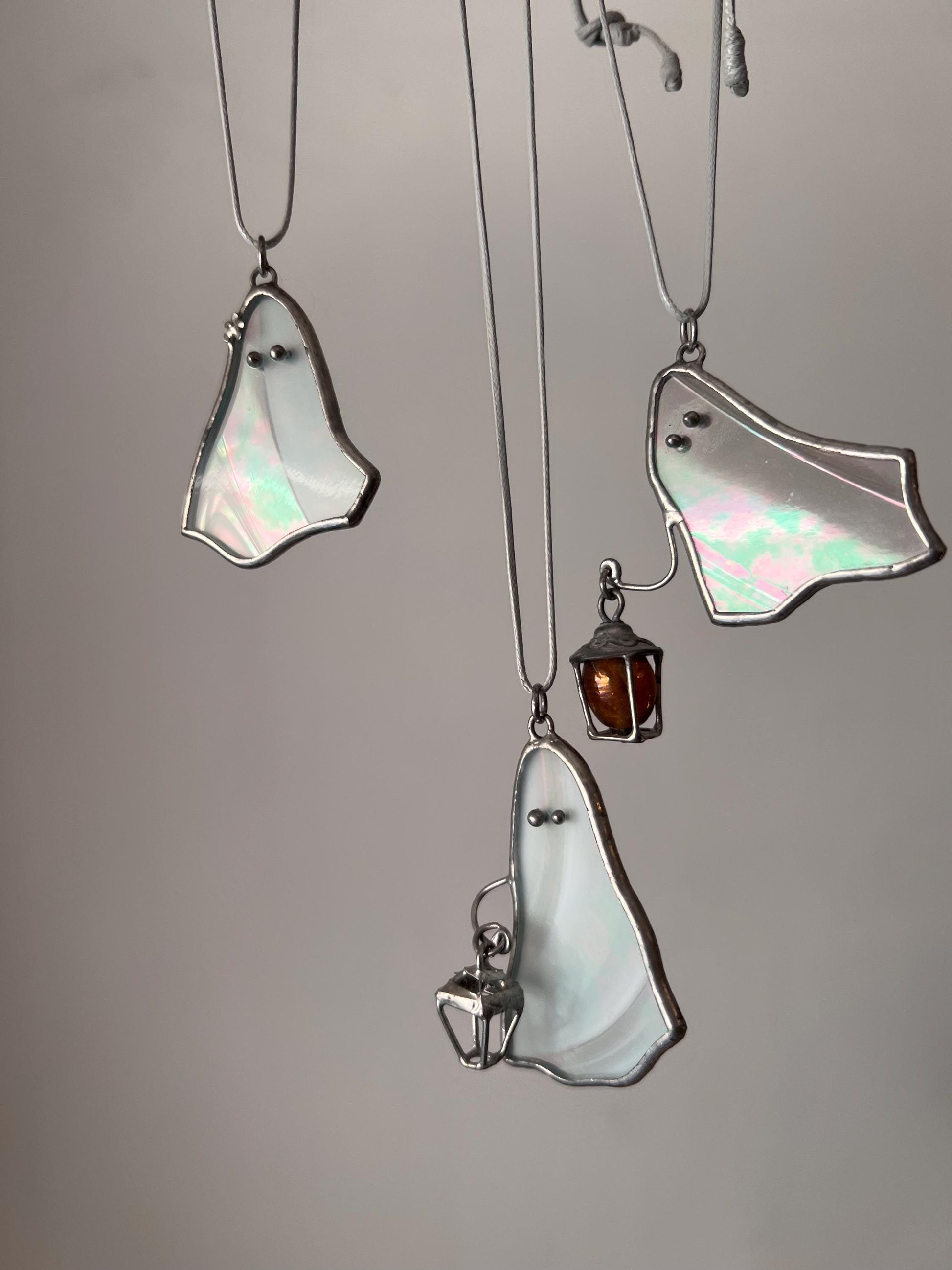 Three white stained glass ghost pendants hanging together, two holding a lantern