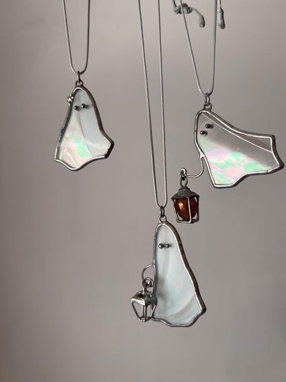 Three white stained glass ghost pendants hanging together, two holding a lantern