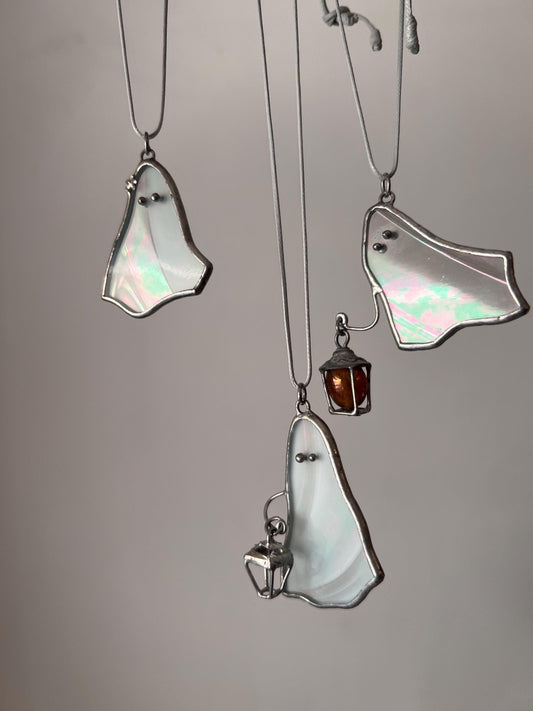 Three white stained glass ghost pendants hanging together, two holding a lantern