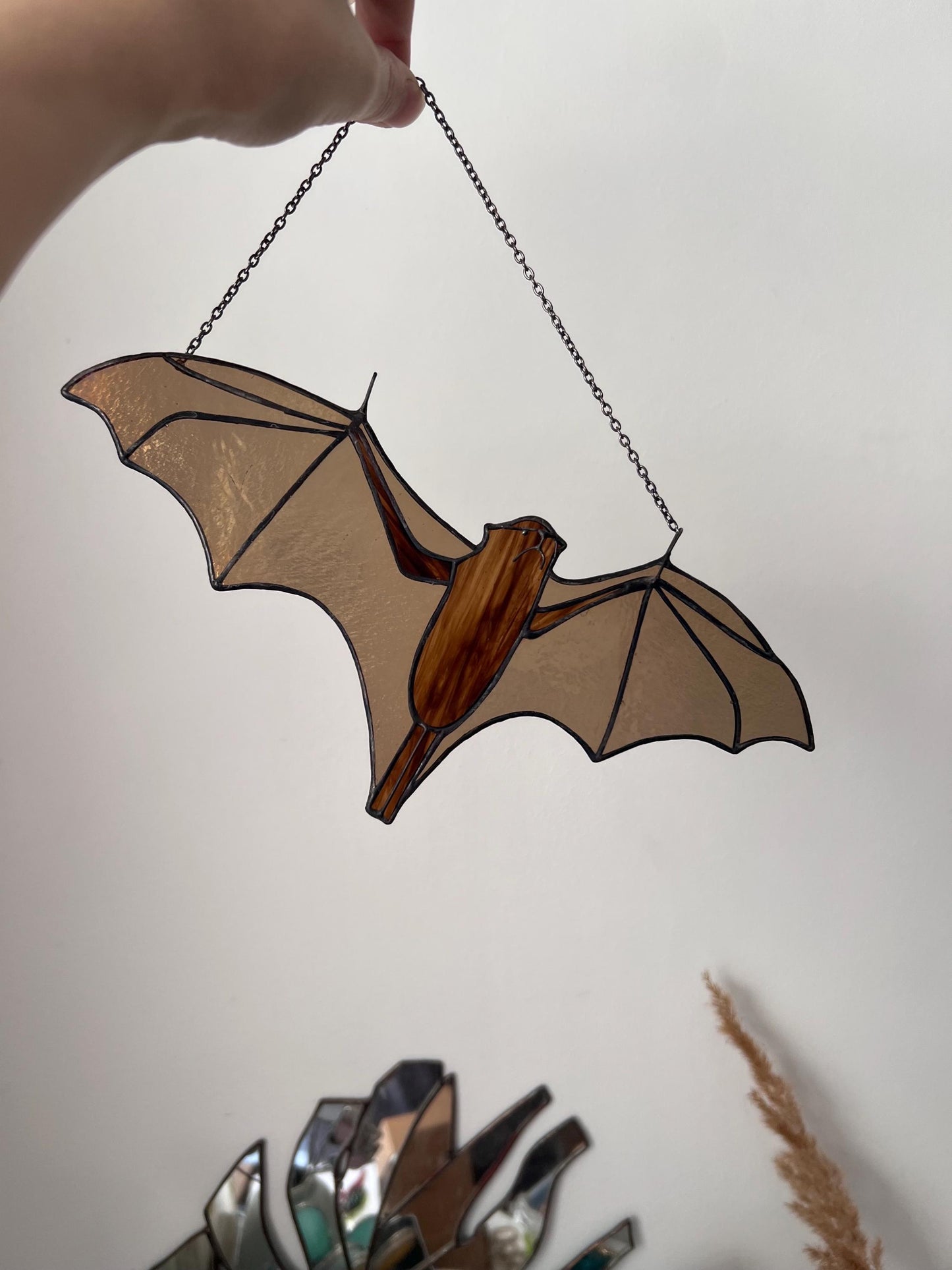 Handmade stained glass decoration in the form of a bat in amber and brown tones hanging on a wall background
