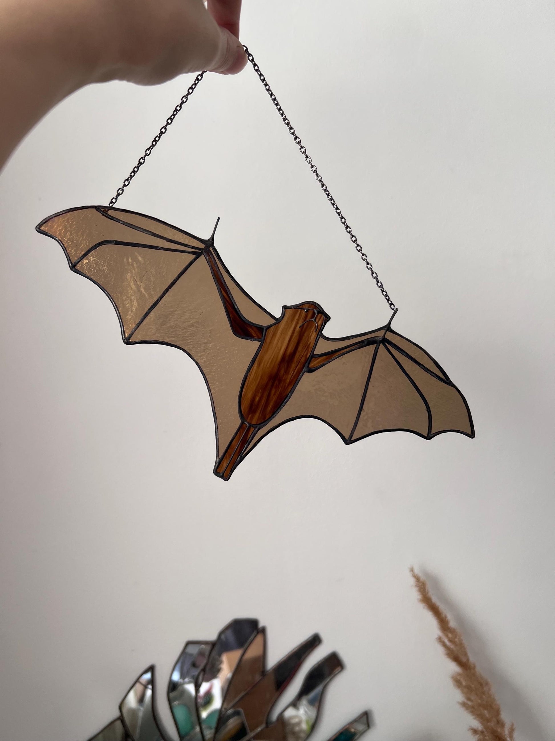 Handmade stained glass decoration in the form of a bat in amber and brown tones hanging on a wall background