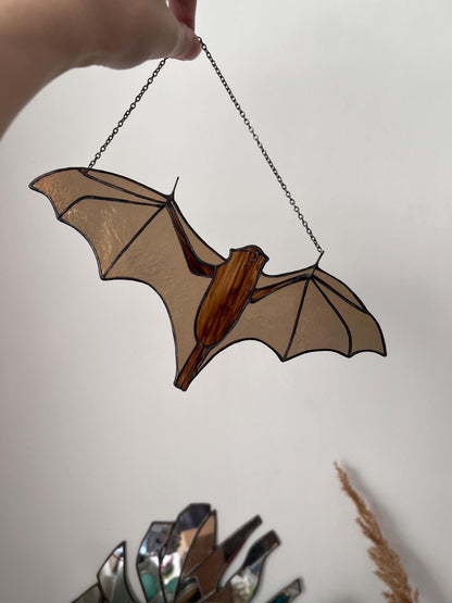 Handmade stained glass decoration in the form of a bat in amber and brown tones hanging on a wall background