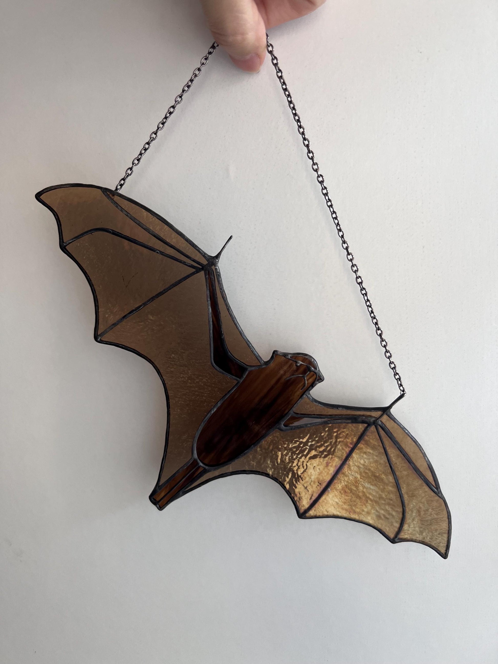 Handmade stained glass decoration in the form of a bat in amber and brown tones hanging on a wall background