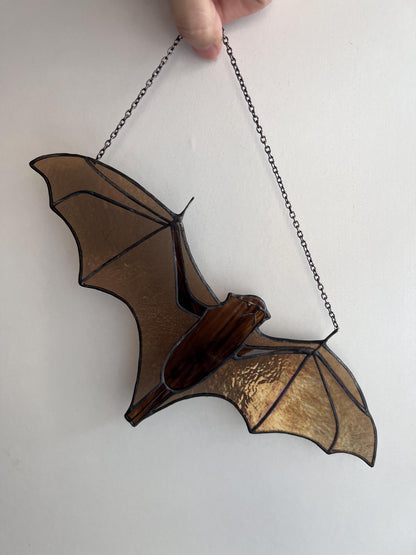 Handmade stained glass decoration in the form of a bat in amber and brown tones hanging on a wall background