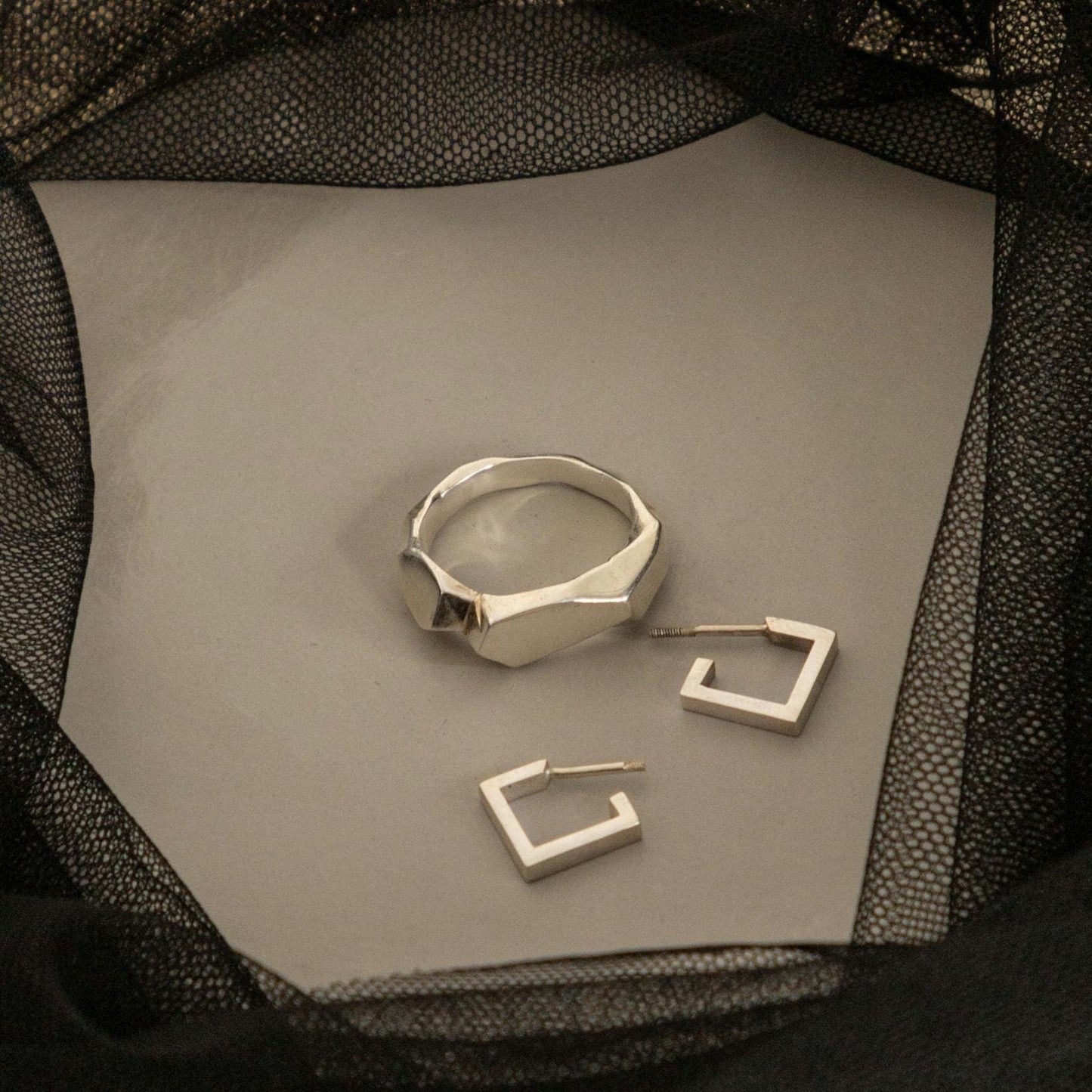 Square silver earrings next to a ring