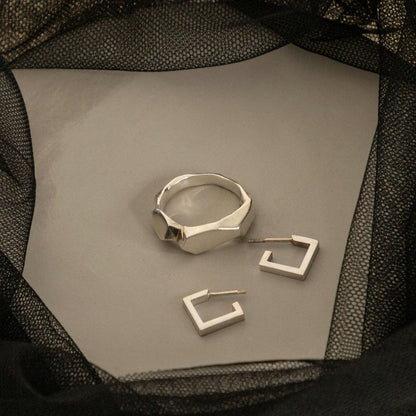 Square silver earrings next to a ring