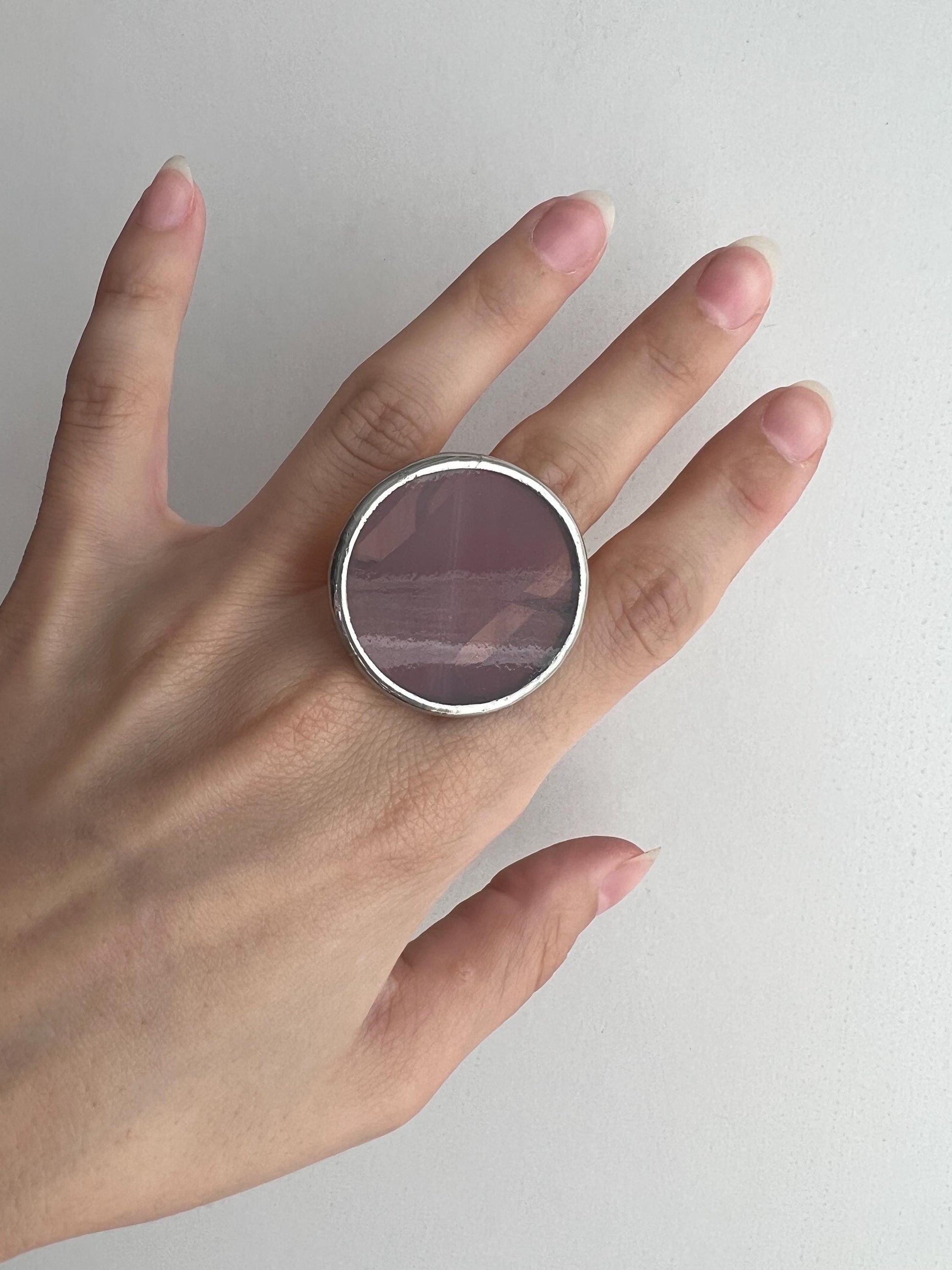 Close-up of plum round stained glass ring on finger