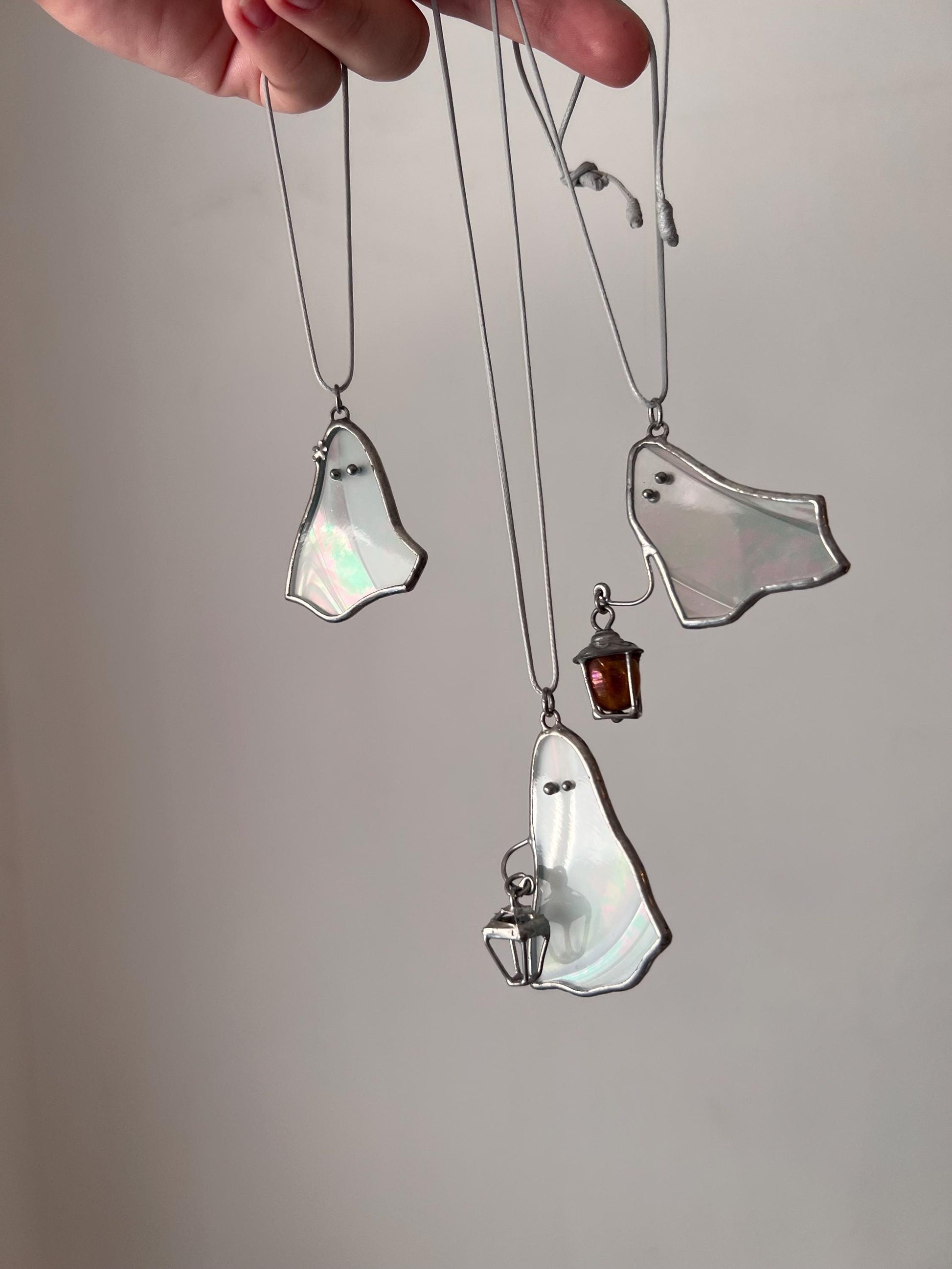 Three white stained glass ghost pendants hanging together, two holding a lantern