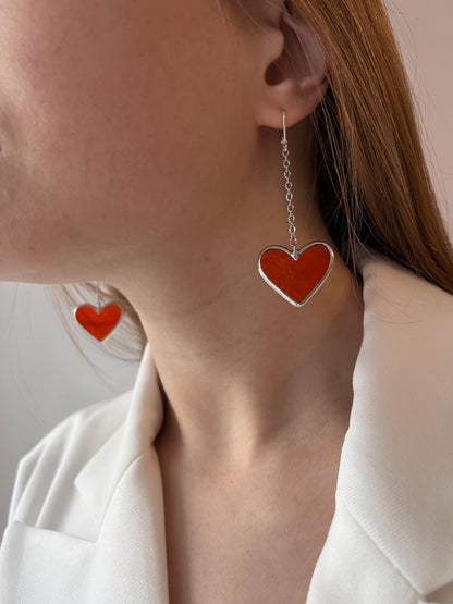 A woman in a white shirt wears long earrings with a red stained glass heart - a modern handmade jewelry.