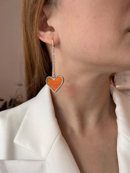 Elegant earrings in the form of red hearts on silver pendants, demonstration on a woman.