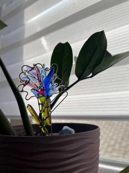 Blue fused glass fantasy flower placed into green houseplant soil