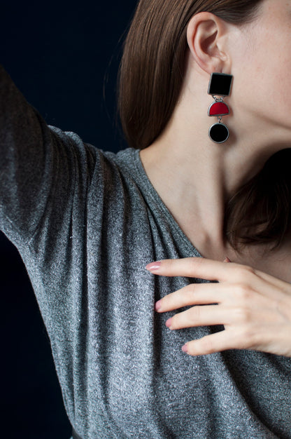 A woman is wearing large geometric glass earrings in black, red and silver.