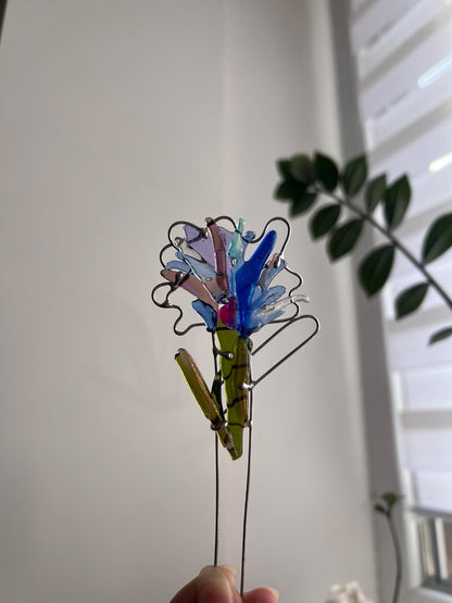 Hand holding red fused glass flower stake against neutral background