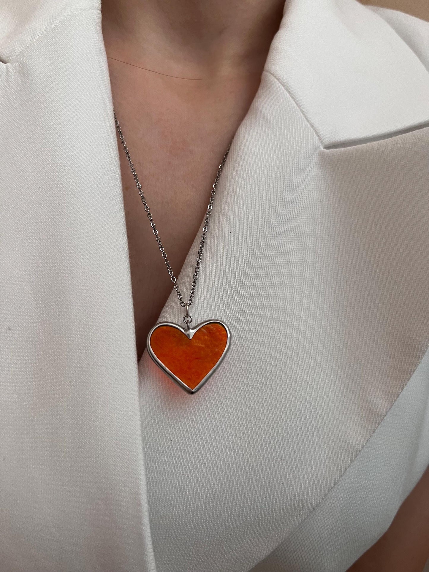 Red glass heart pendant on the neck of a model in a white blouse.