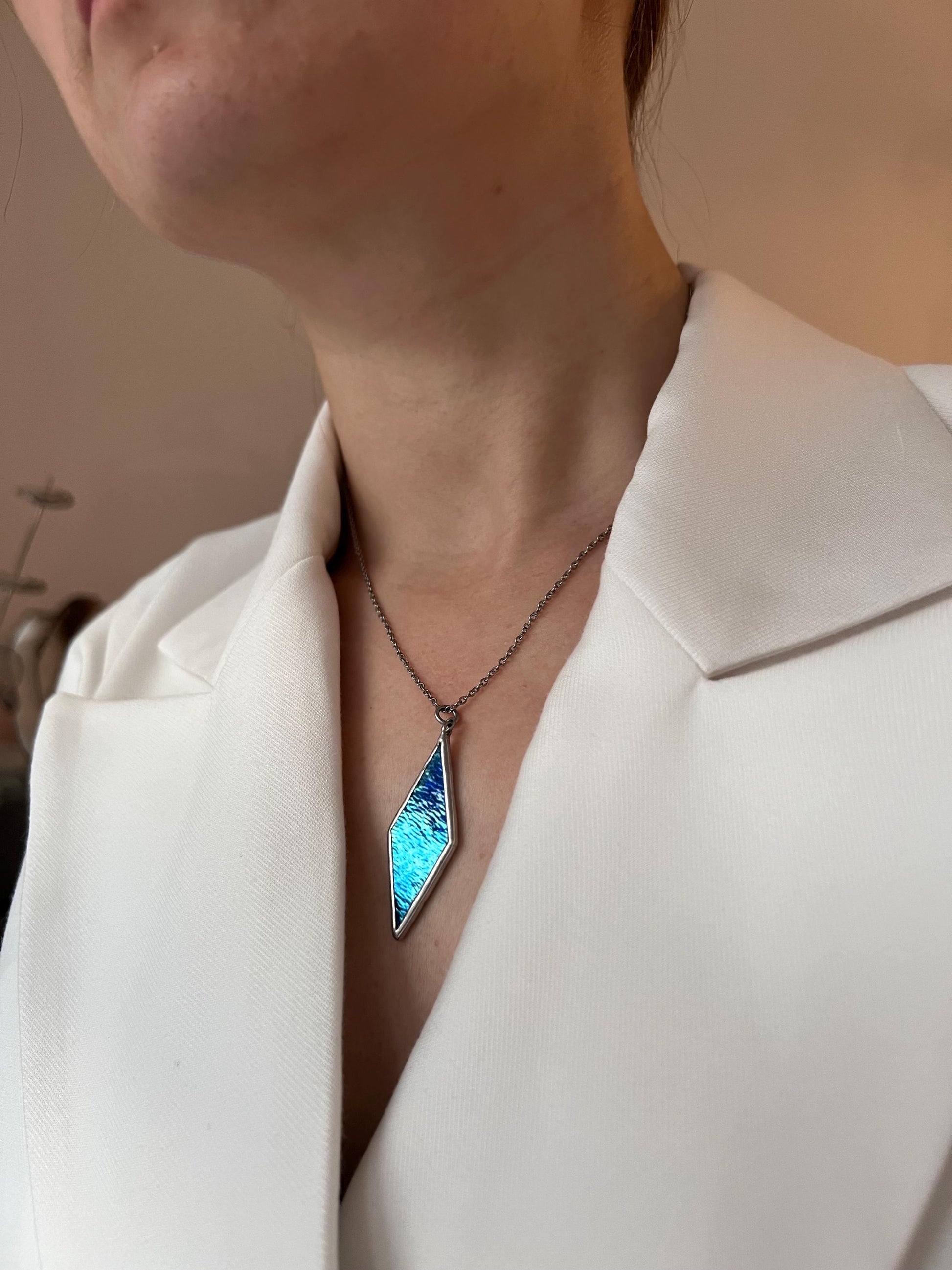 A woman in a light shirt wears a blue diamond pendant, a modern handmade decoration.