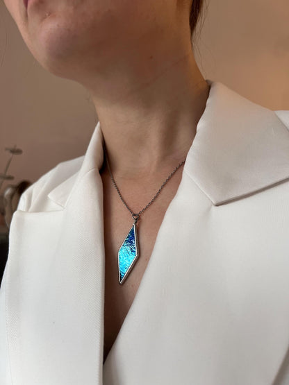 A woman in a light shirt wears a blue diamond pendant, a modern handmade decoration.