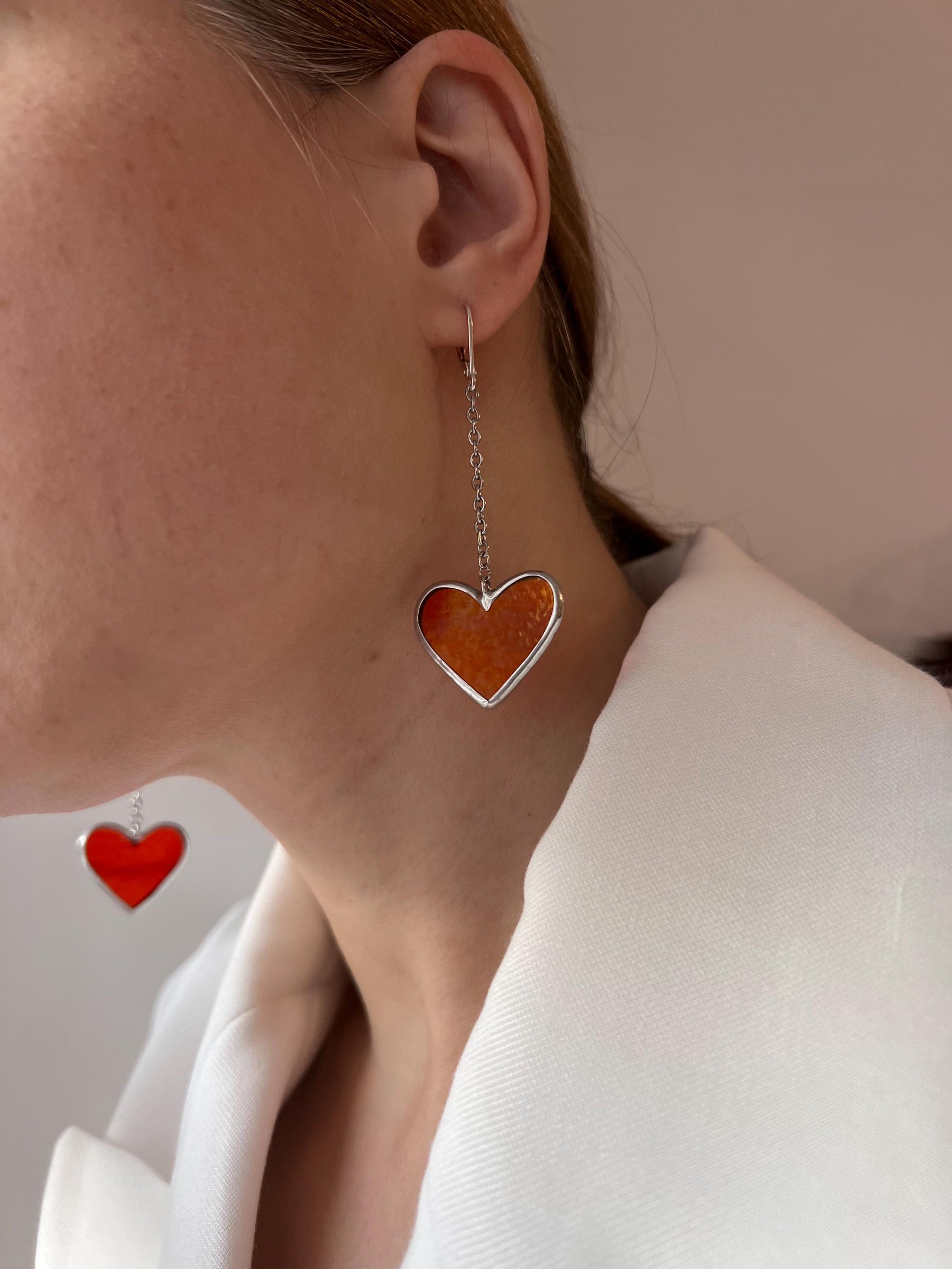 An earring with a red glass heart on a long silver hook, side view on a model.