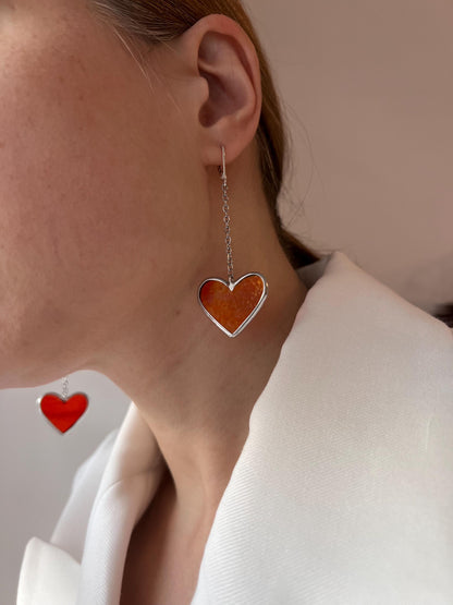 An earring with a red glass heart on a long silver hook, side view on a model.