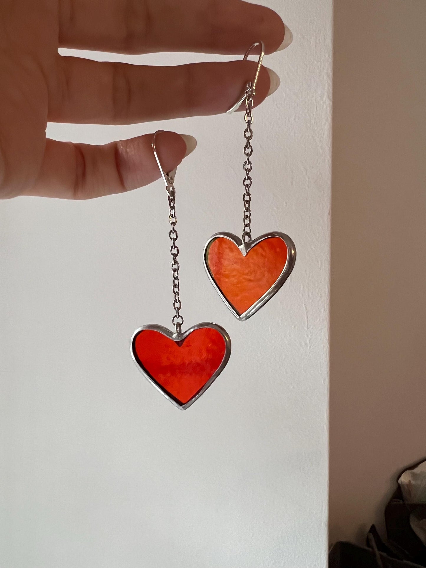 Earrings in the form of stained glass hearts on the palm of her hand, a stylish handmade accessory.