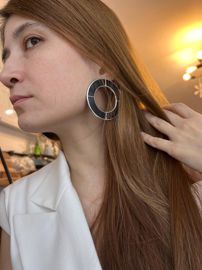 Model adjusting hair while wearing black geometric statement earrings