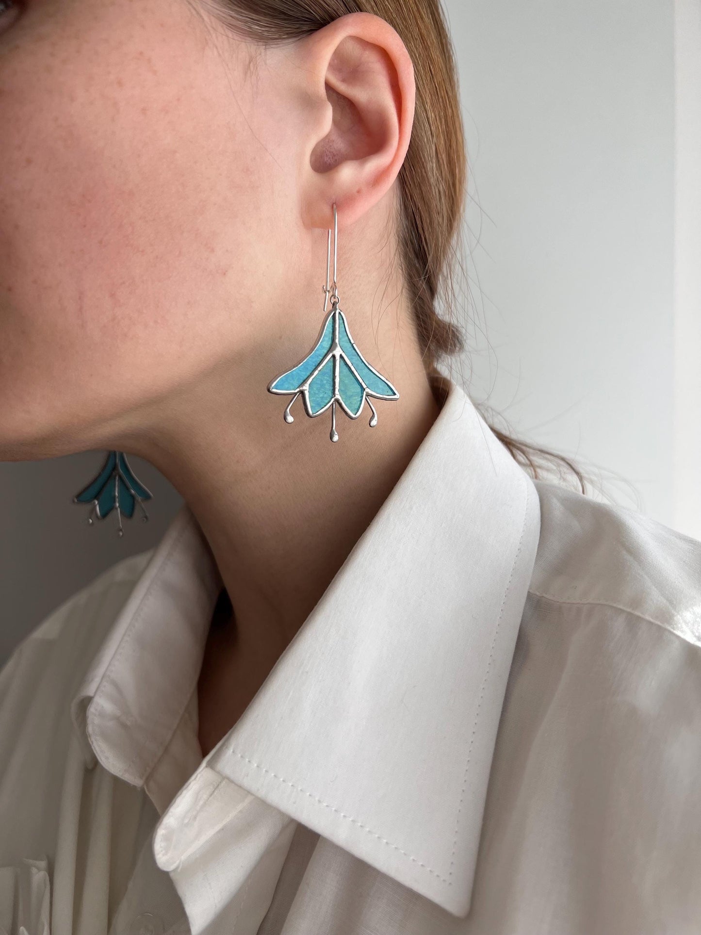 Handmade turquoise blue stained glass earrings shaped like bluebell flowers.