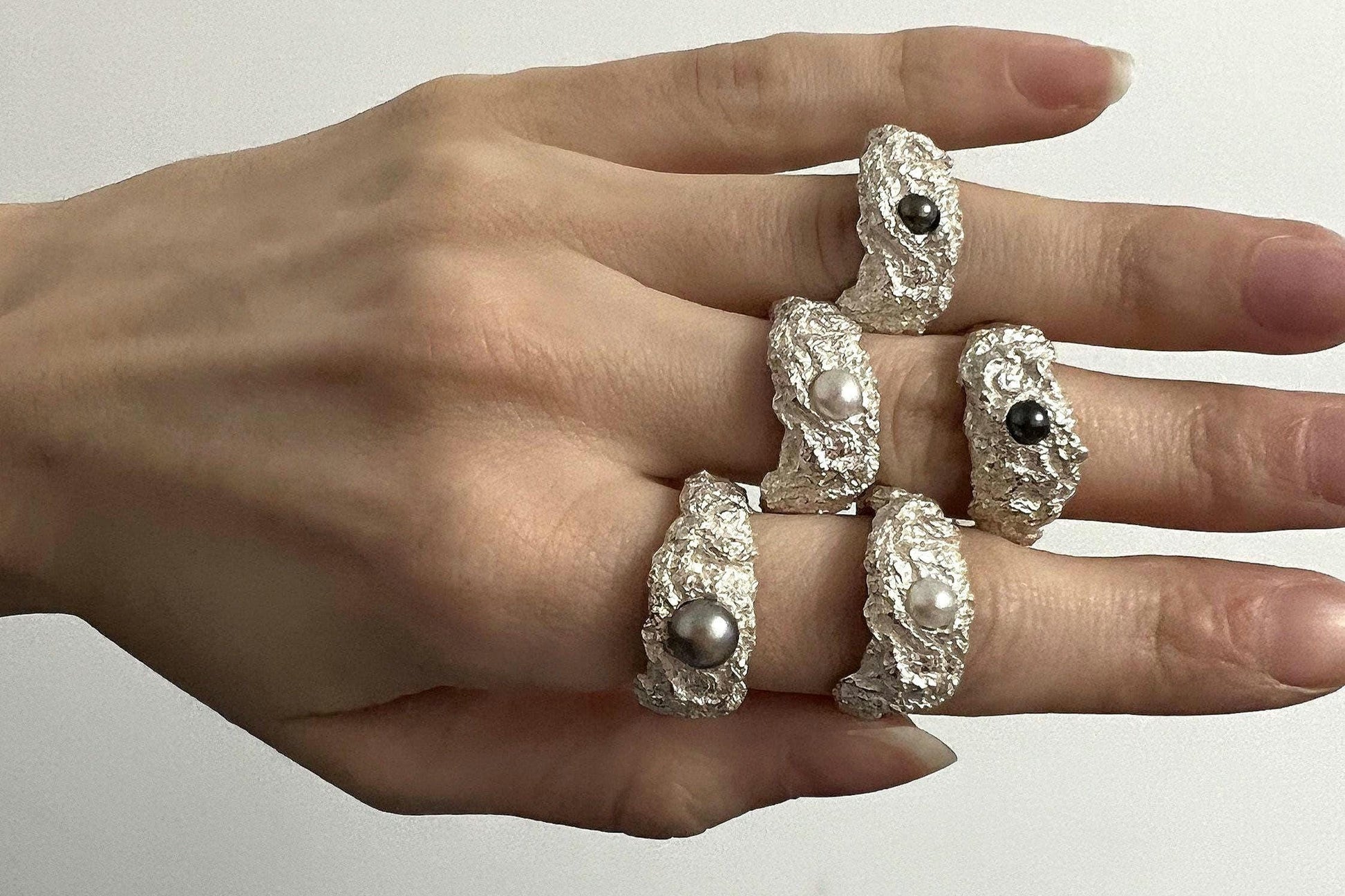 Hand wearing textured silver ring with white pearl, artisan jewelry