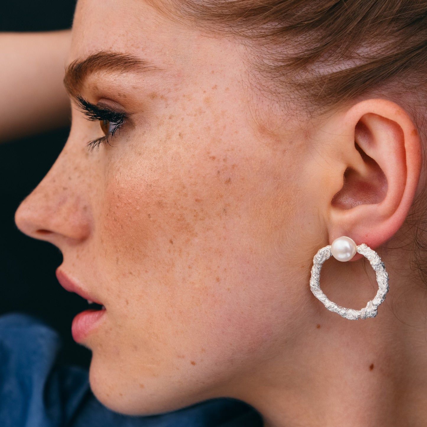 Handmade silver pearl hoop earrings on blue background