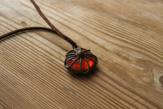 Red handmade glass pendant with copper wire detail on wooden background