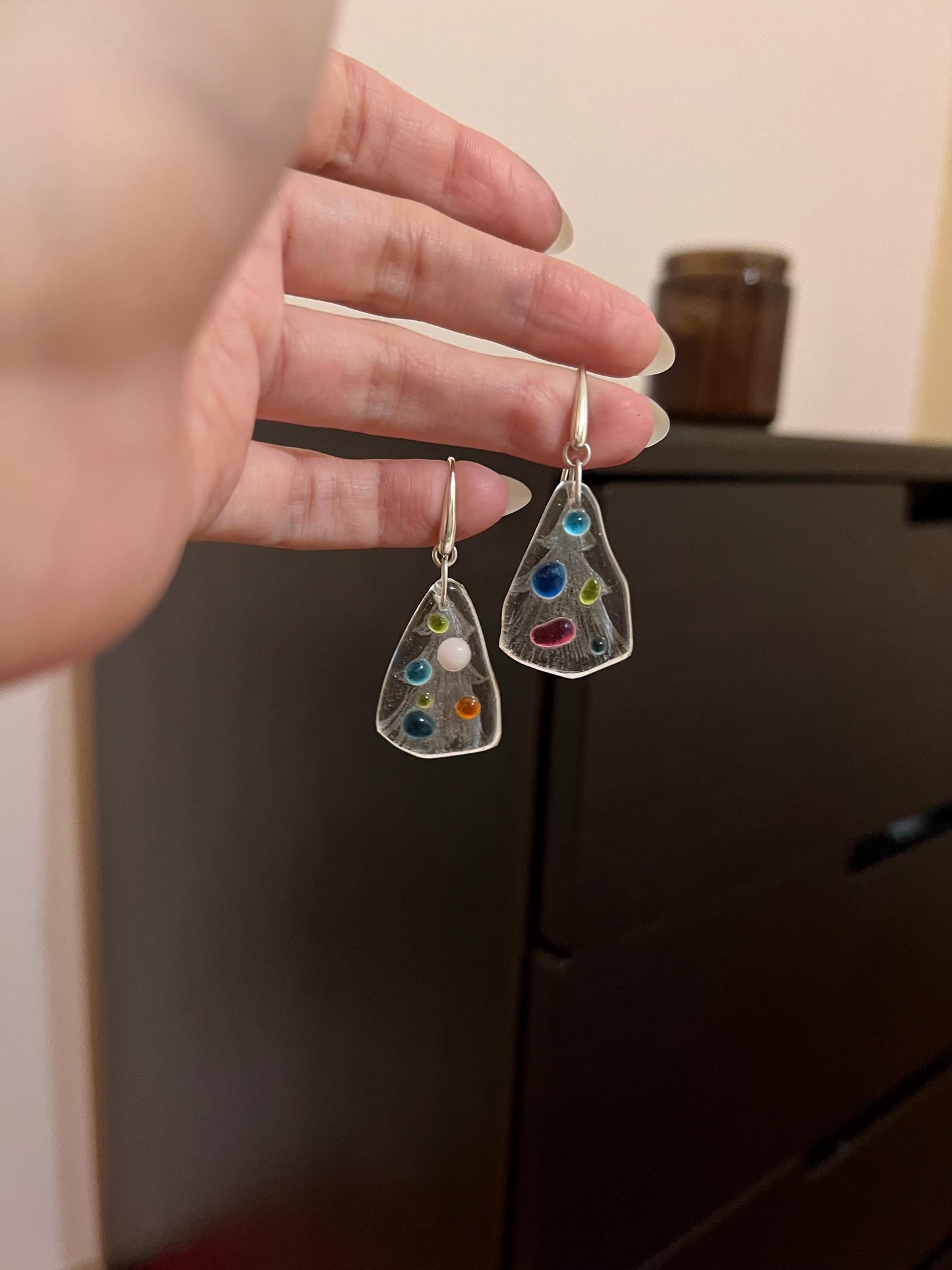 Hand holding fused glass holiday tree earrings with colorful dots