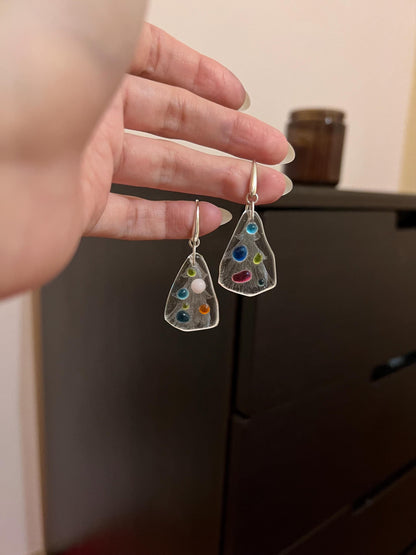 Hand holding fused glass holiday tree earrings with colorful dots