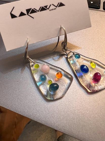 Close-up of handmade fused glass tree earrings on a silver surface