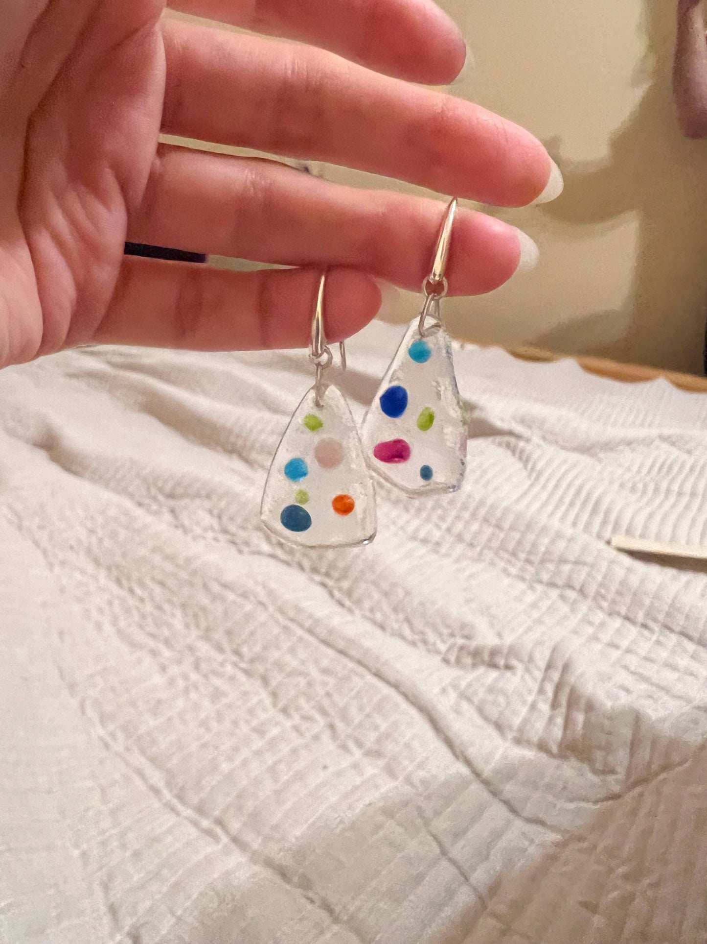 Earrings held over light fabric background showing colors clearly