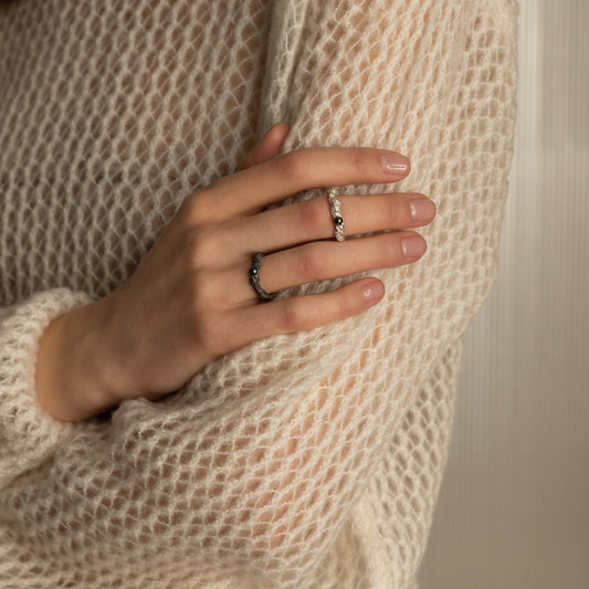 Hand wearing textured sterling silver ring with white pearl, minimalist design on knitted sweater background