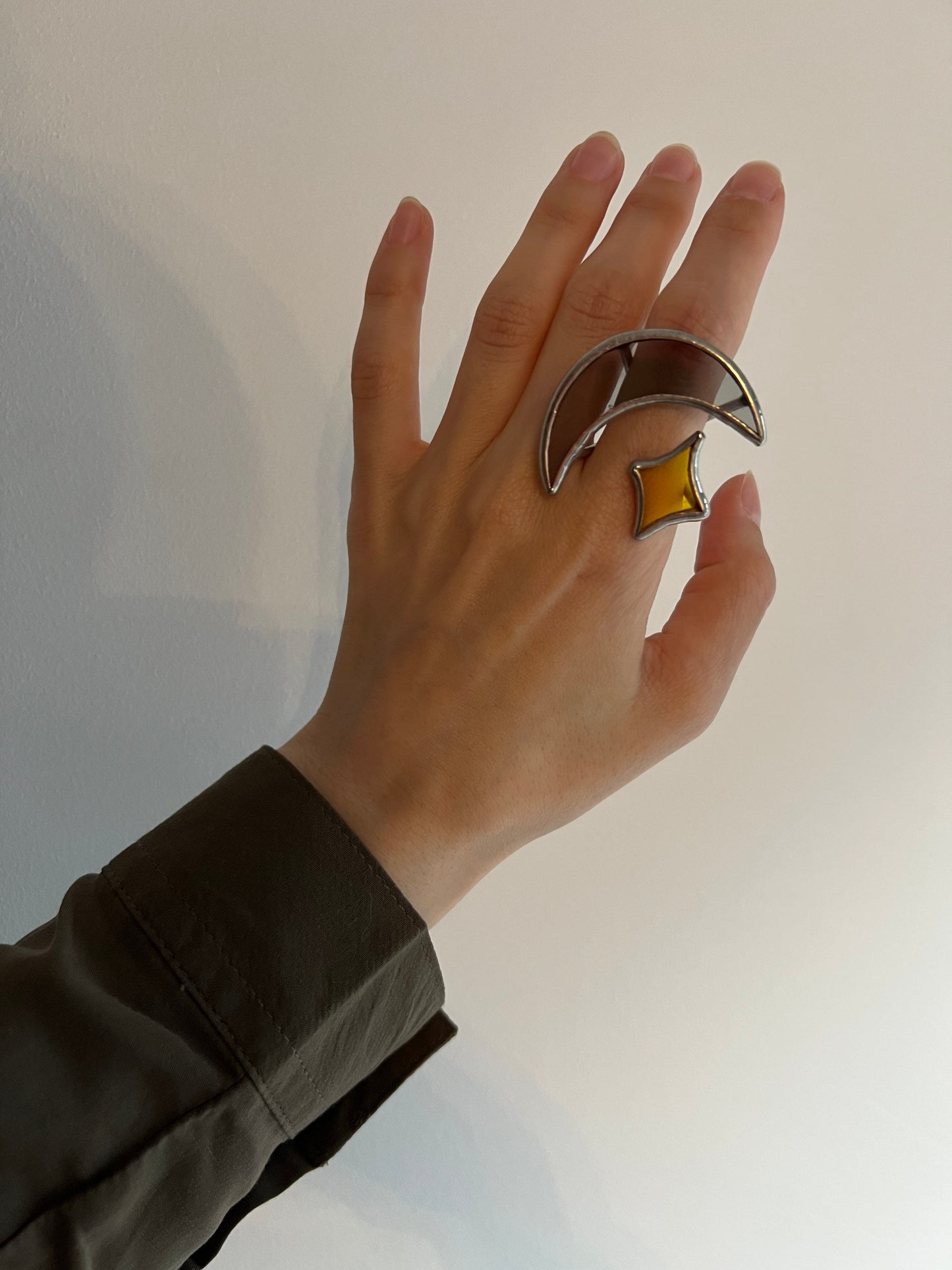 Hand wearing chunky stained glass moon and star ring, close-up on white background