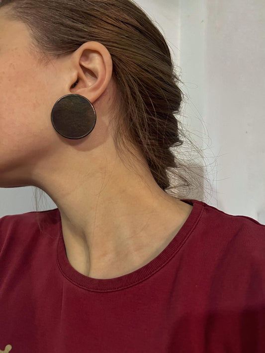 Model wearing large round black iridescent studs