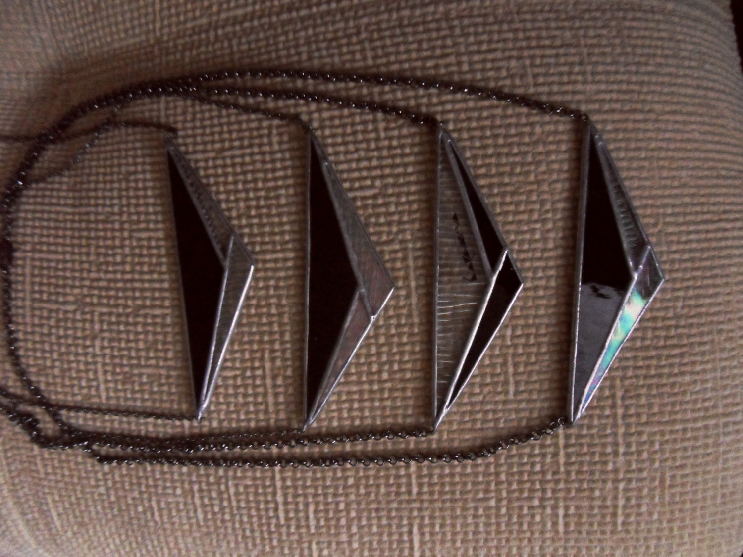 Four stained glass triangle pendants in a row on fabric.