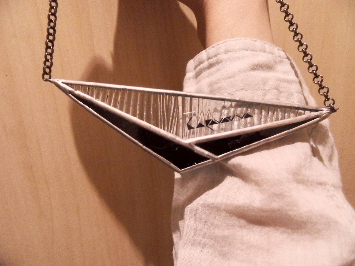 a large horizontal pendant in the shape of a triangle made of black and transparent glass, lying on the model's hand, the texture and chain are clearly visible.